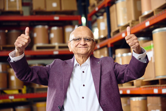 Nitin Shah, CEO, giving a thumbs-up in a warehouse setting with shelves of boxes.